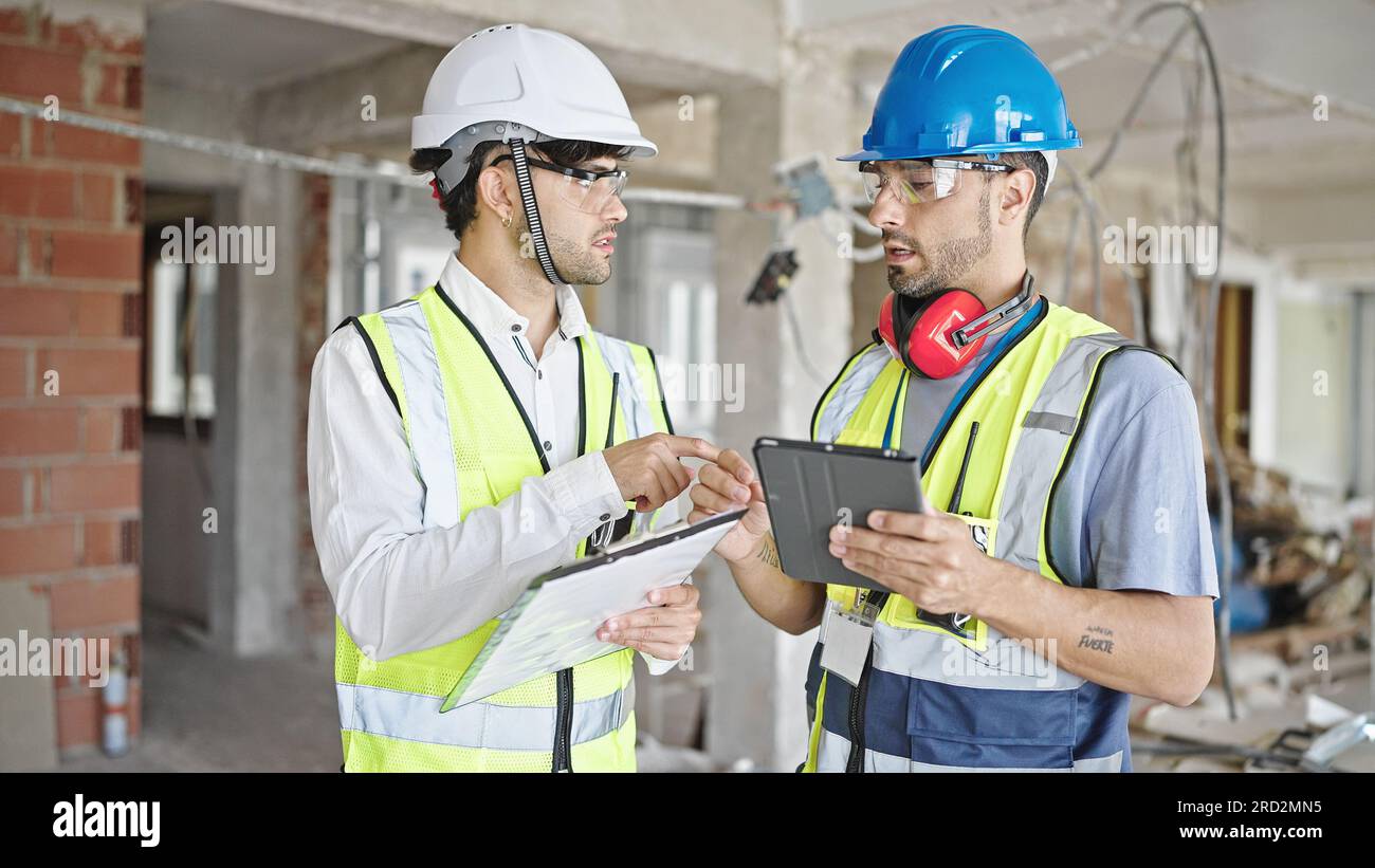 Two men builders and architect using touchpad shake hands at construction site Stock Photo