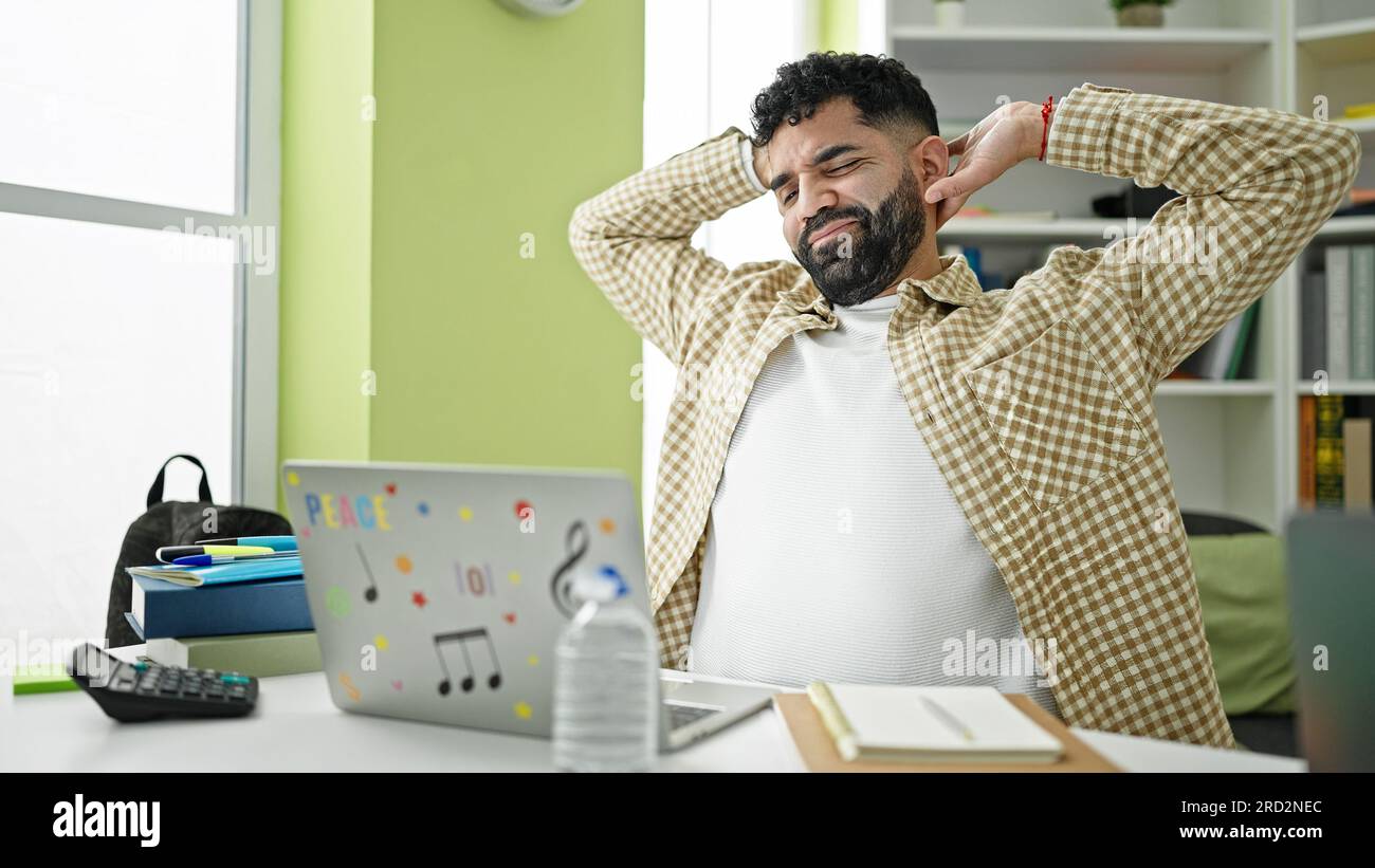 Young hispanic man student using laptop stretching back at library university Stock Photo