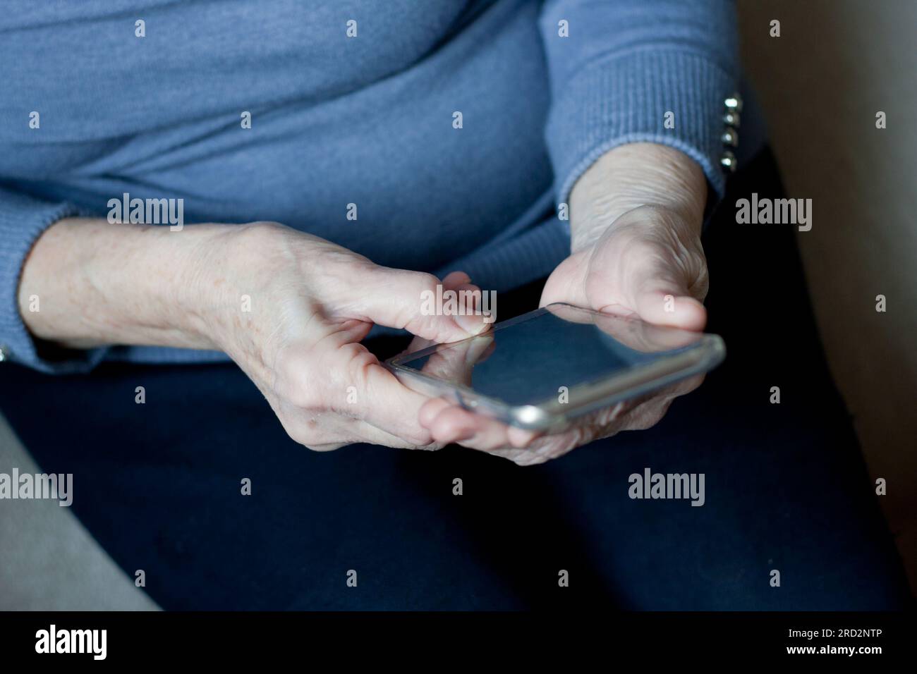 hands of an senior woman holding an smartphone in hands. Closeup, elderly man uses smartphone, touches screen of mobile phone with his finger. Telecom Stock Photo