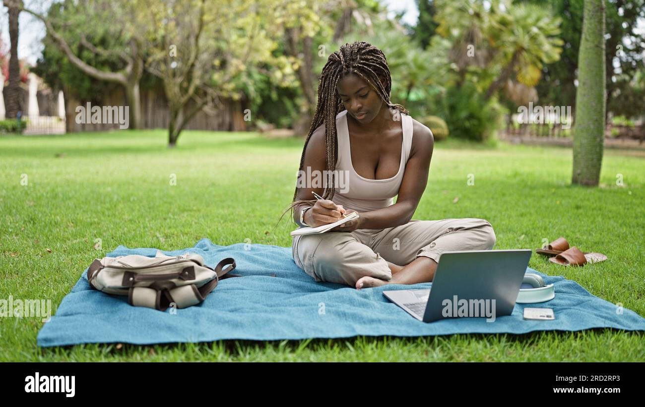 African american woman student using laptop taking notes at campus ...