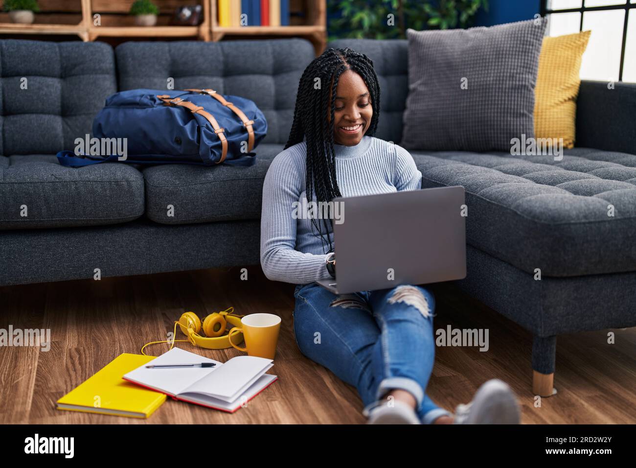 African american woman student sitting on floor using laptop at street ...