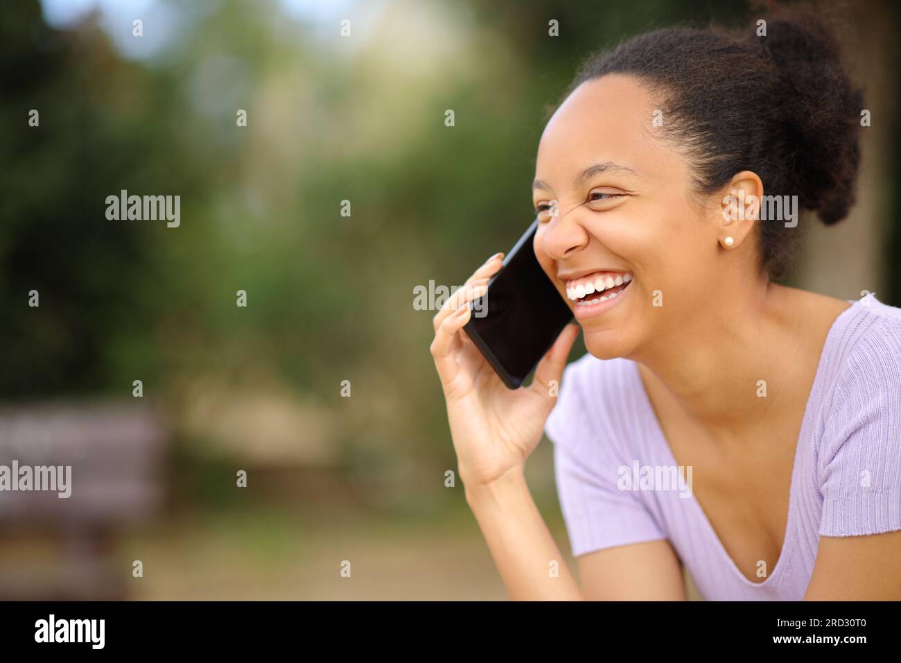 Happy black woman talking on phone laughing in a park Stock Photo