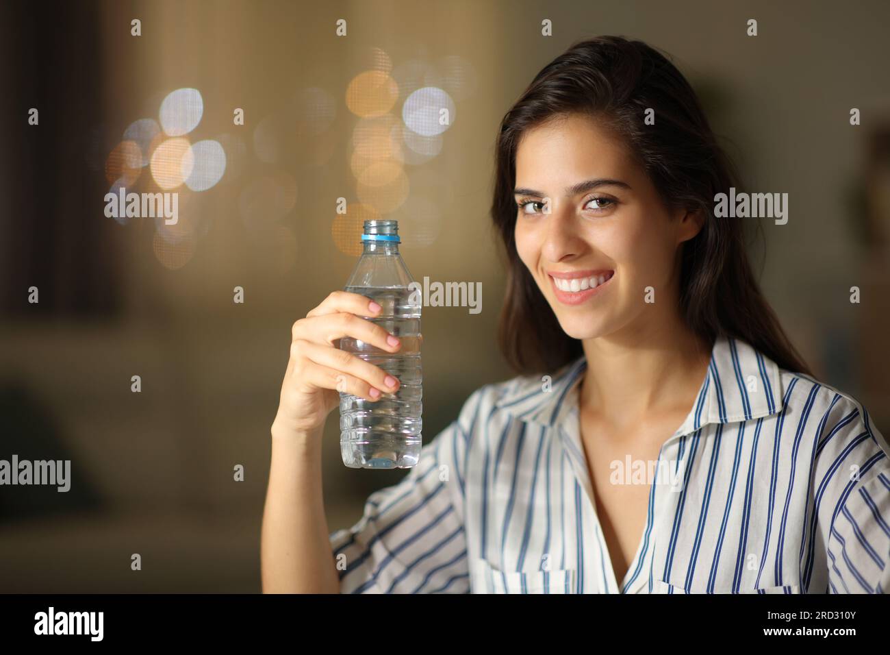 https://c8.alamy.com/comp/2RD310Y/happy-woman-posing-holding-water-bottle-looking-at-camera-at-home-in-the-night-2RD310Y.jpg