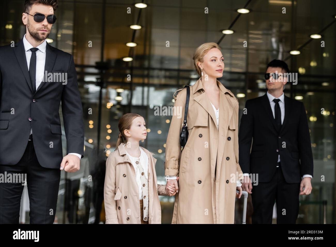 bodyguards walking next to blonde successful woman and preteen kid, entering hotel, private security, mother and daughter in trench coats, safety and Stock Photo