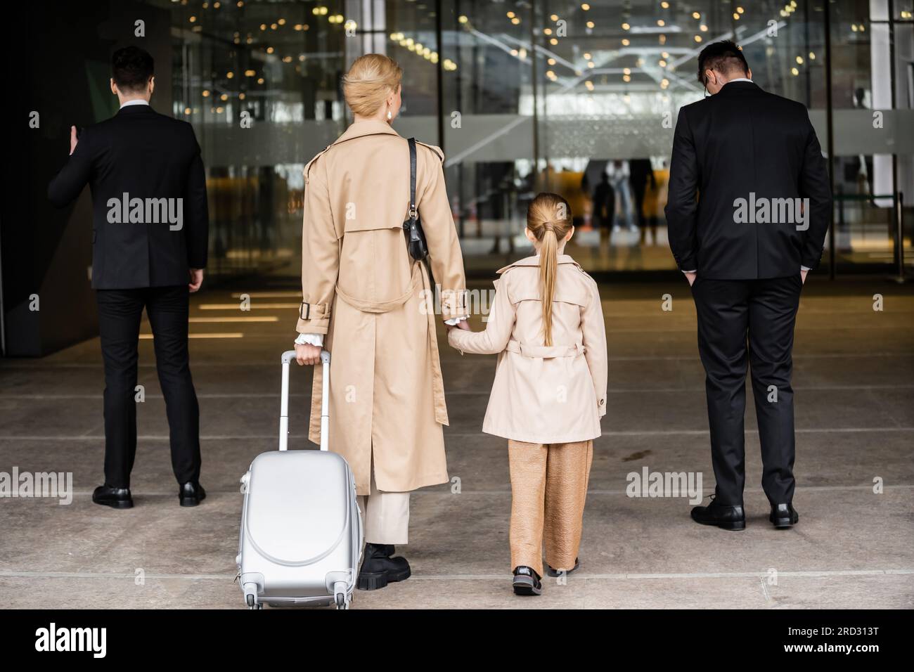 back view of two bodyguards walking next to blonde woman and preteen ...