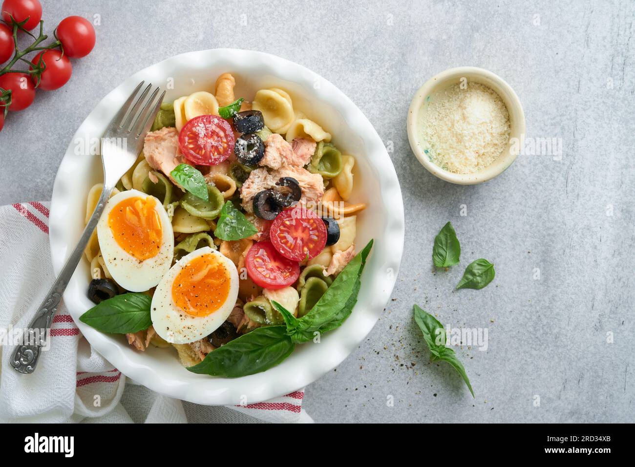Italian pasta salad. Orecchiette pasta with tuna, tomato cherry, olive, basil and parmesan cheese in plate on grey stone or concrete background. Tradi Stock Photo