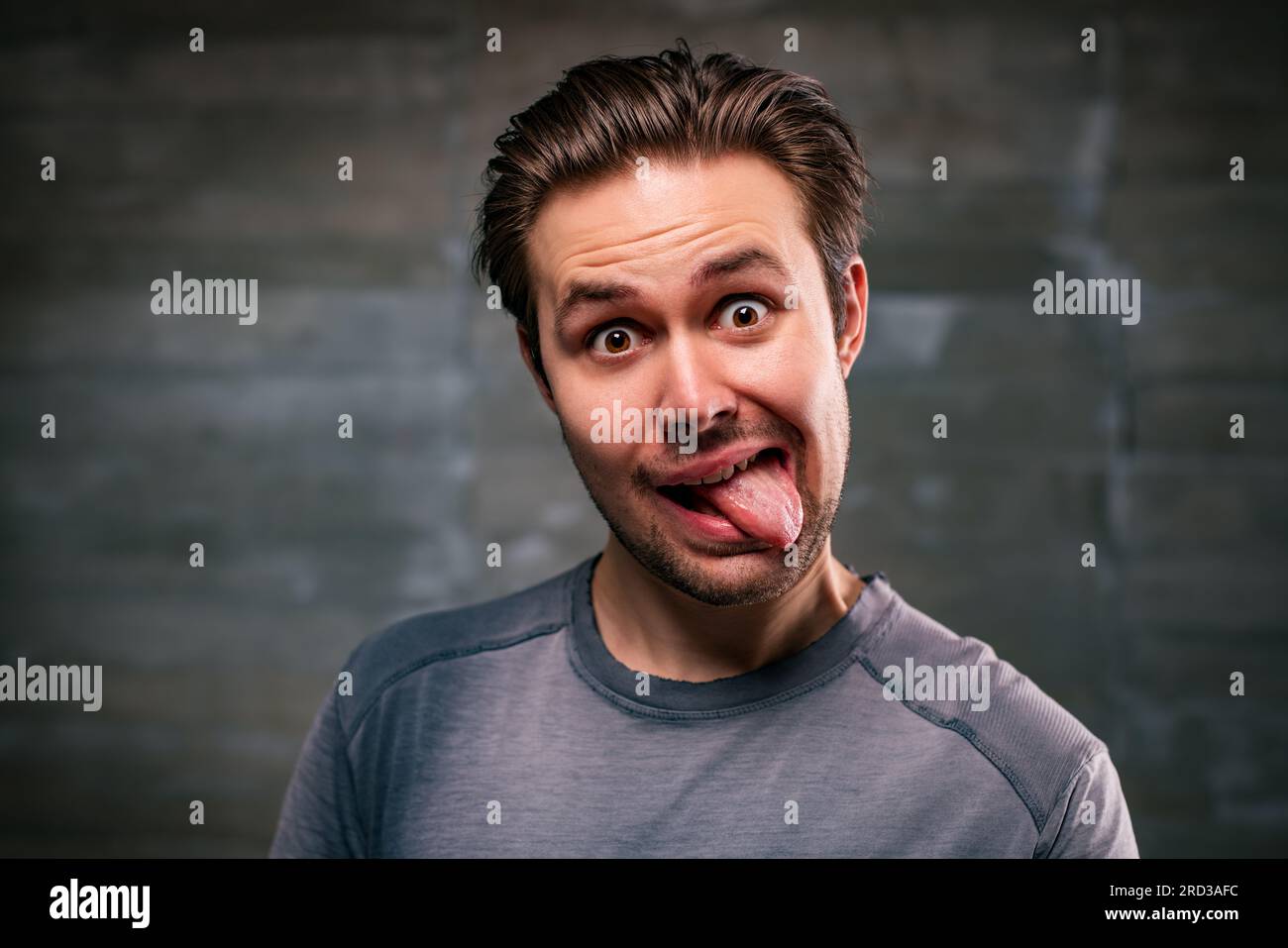 Young man showing tongue portrait on gray wall background Stock Photo