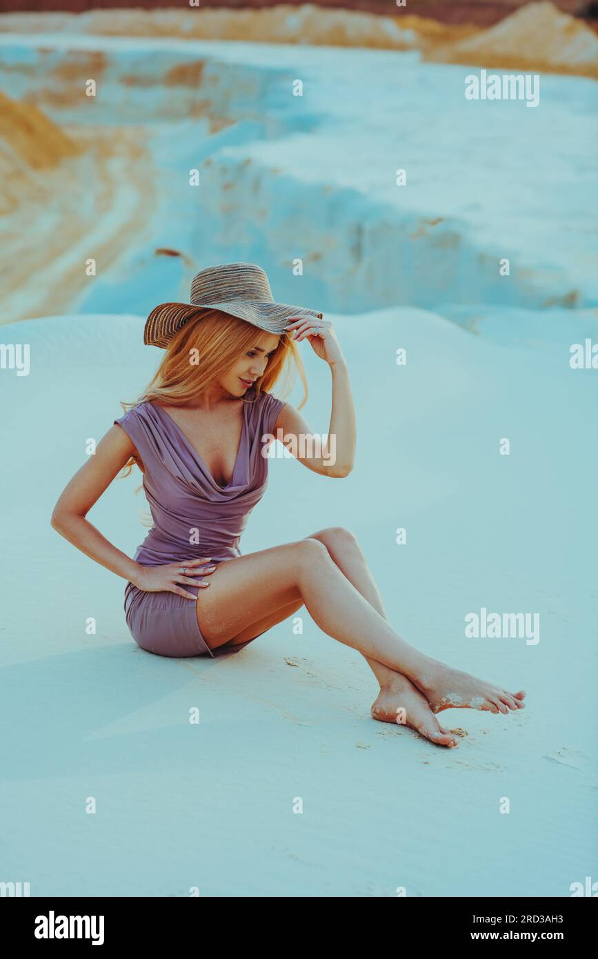 Young slim woman with hat sitting on sand at desert landscape Stock Photo