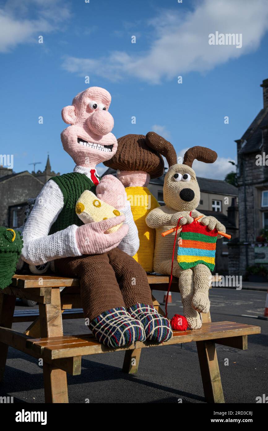 Hawes, North Yorkshire. 17 July 2023. The Hawes Yarnbombers, a local group of extreme knitters, unveiled their latest creation in the market town of Hawes in the heart of the Yorkshire Dales. The larger than life knitted figures of Wallace and Gromit, along with other characters from the series, take up several benches, and see Wallace with a big wedge of Wensleydale cheese, which is his favorite, and is famously made in the Wensleydale Creamery based in Hawes. Donations for the artwork are given to the Yorkshire Air Ambulance Service. Credit: Wayne HUTCHINSON/Alamy Live News Stock Photo