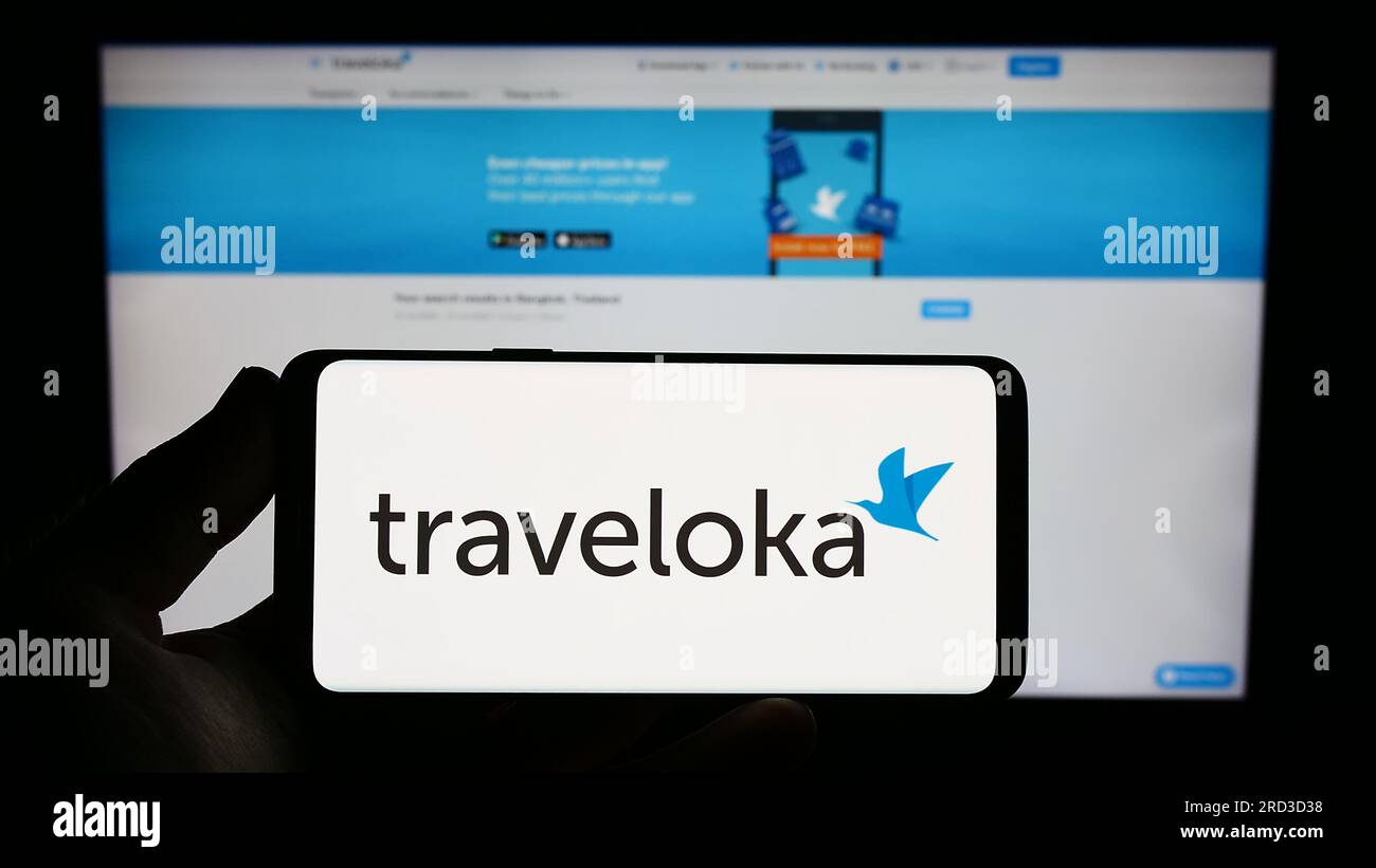 Person holding smartphone with logo of Indonesian travel company Traveloka on screen in front of website. Focus on phone display. Stock Photo
