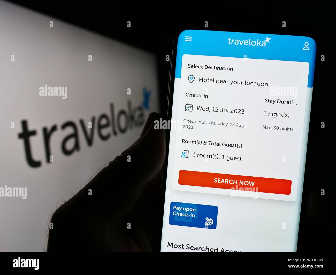 Person holding cellphone with webpage of Indonesian travel company Traveloka on screen in front of logo. Focus on center of phone display. Stock Photo