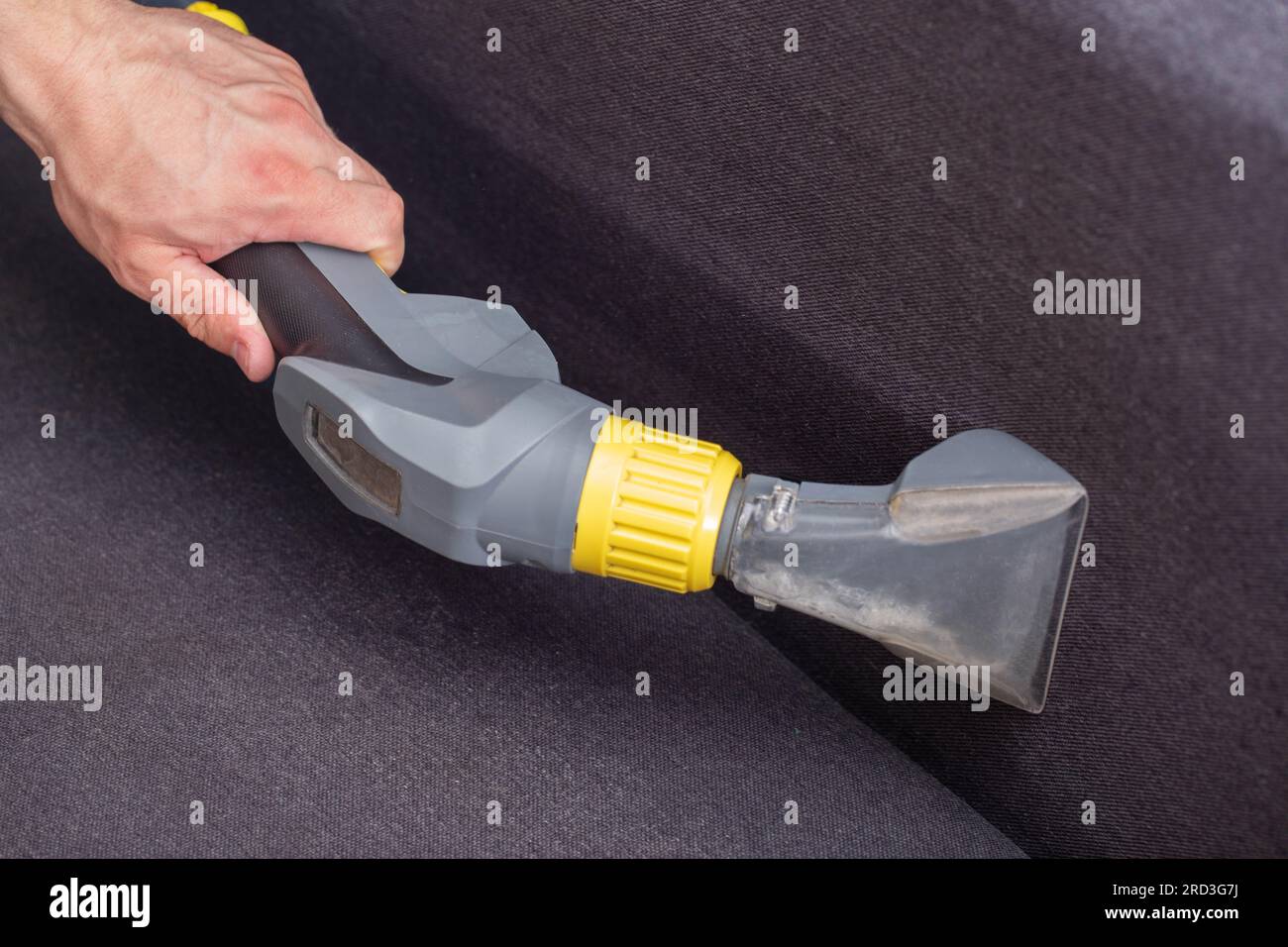 Dry cleaning of the black upholstery on the sofa with a special washing vacuum cleaner. Stock Photo