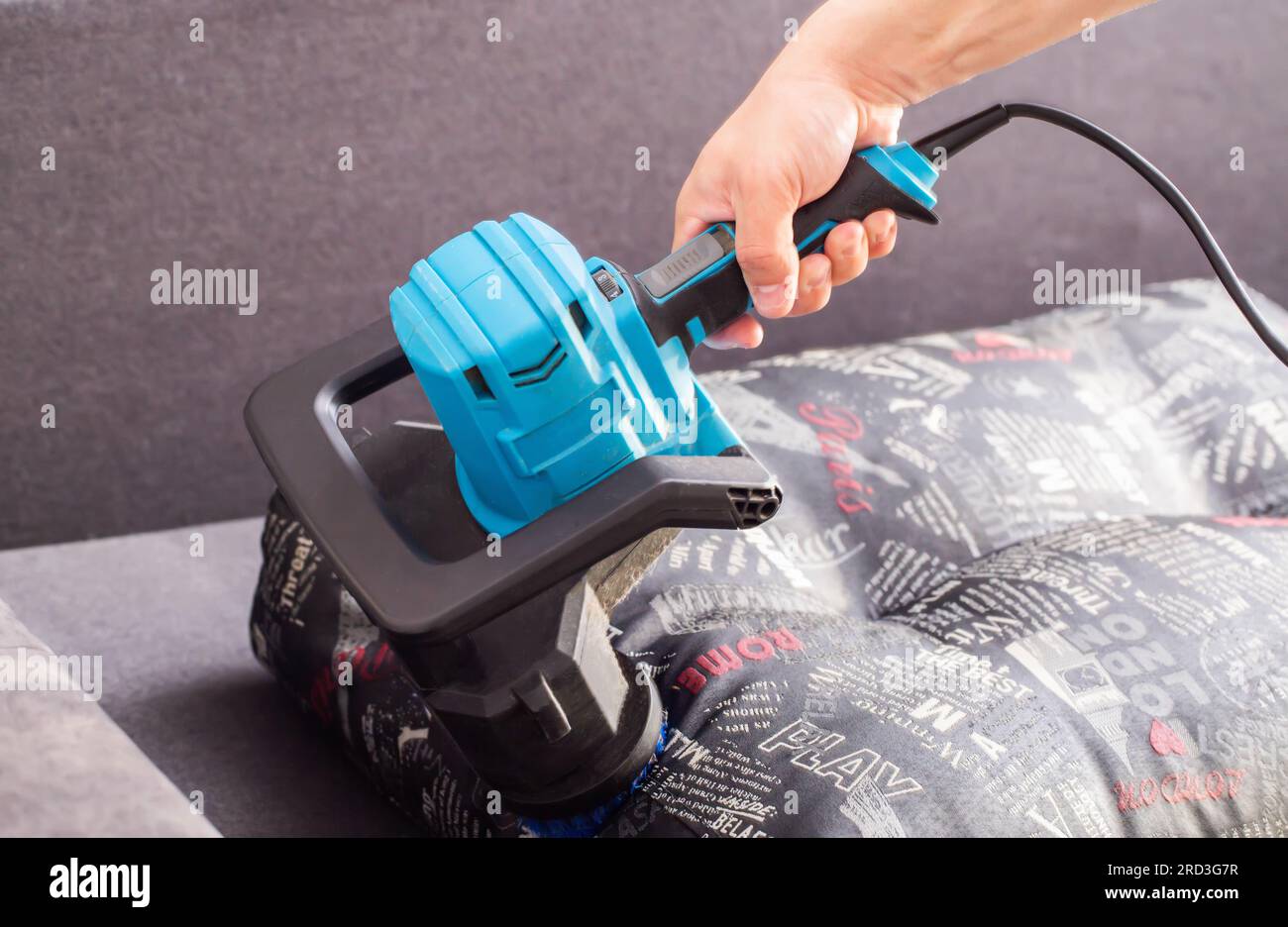 Cleaning sofa cushions with a special electric brush. Dry cleaning of upholstered furniture, close-up. Stock Photo
