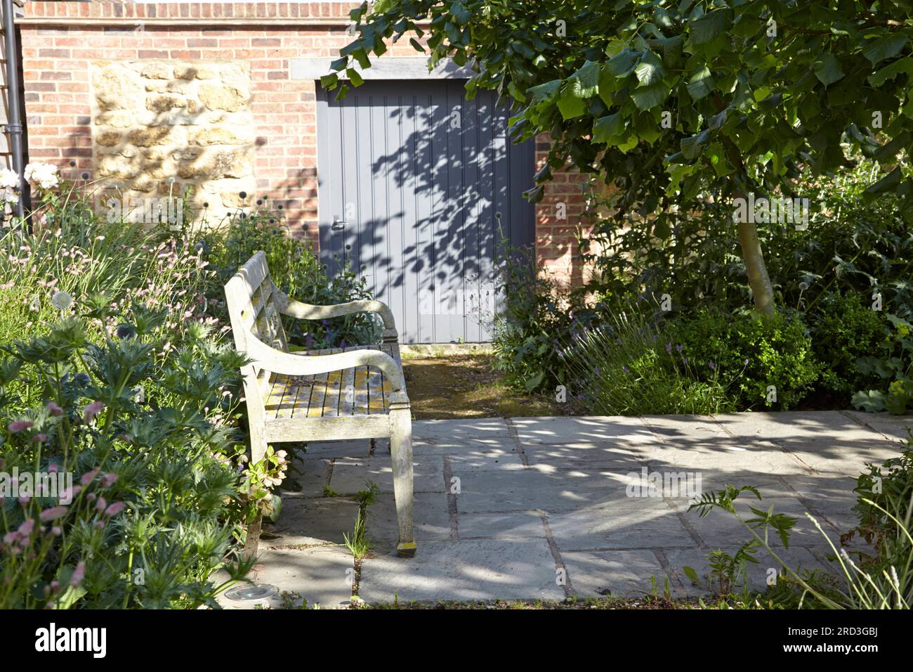 Wood garden bench on paved area in front of stone wall with door. Manor