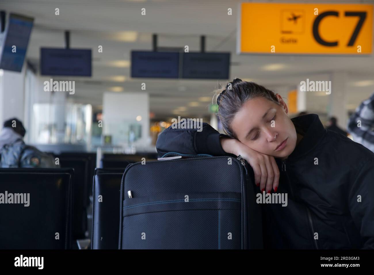 Tired tourist woman sleeping on luggage while waiting for her flight at