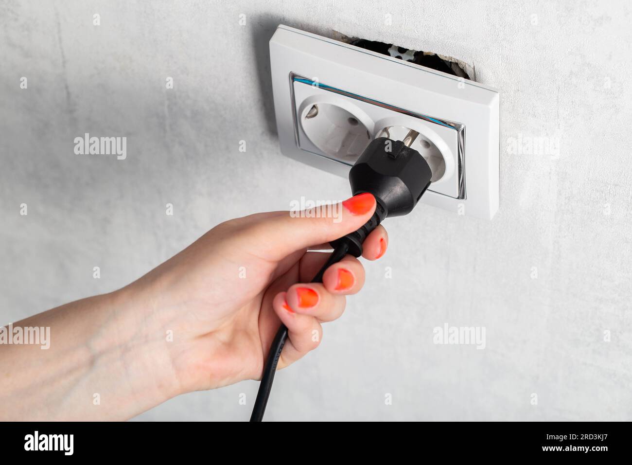 The girl puts the electric plug into a broken socket. Risk of electric