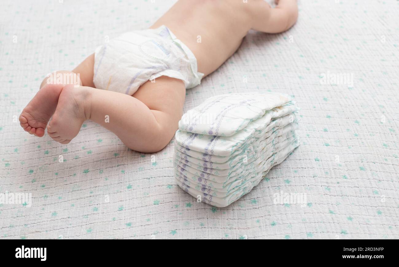 The legs of a baby in a diaper against the background of a stack of children's comfortable
