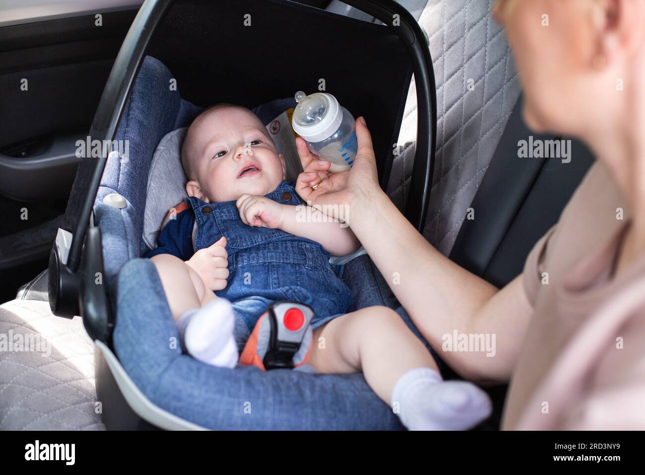 mother feeds the baby in, car seat in the car, milk from a bottle