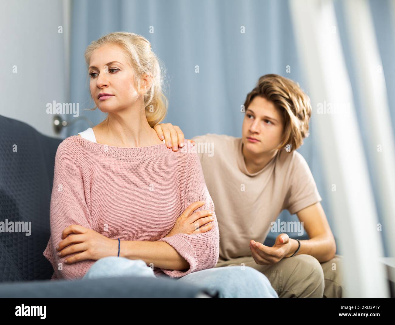 Upset woman sitting at home while teenage son calming her Stock Photo ...