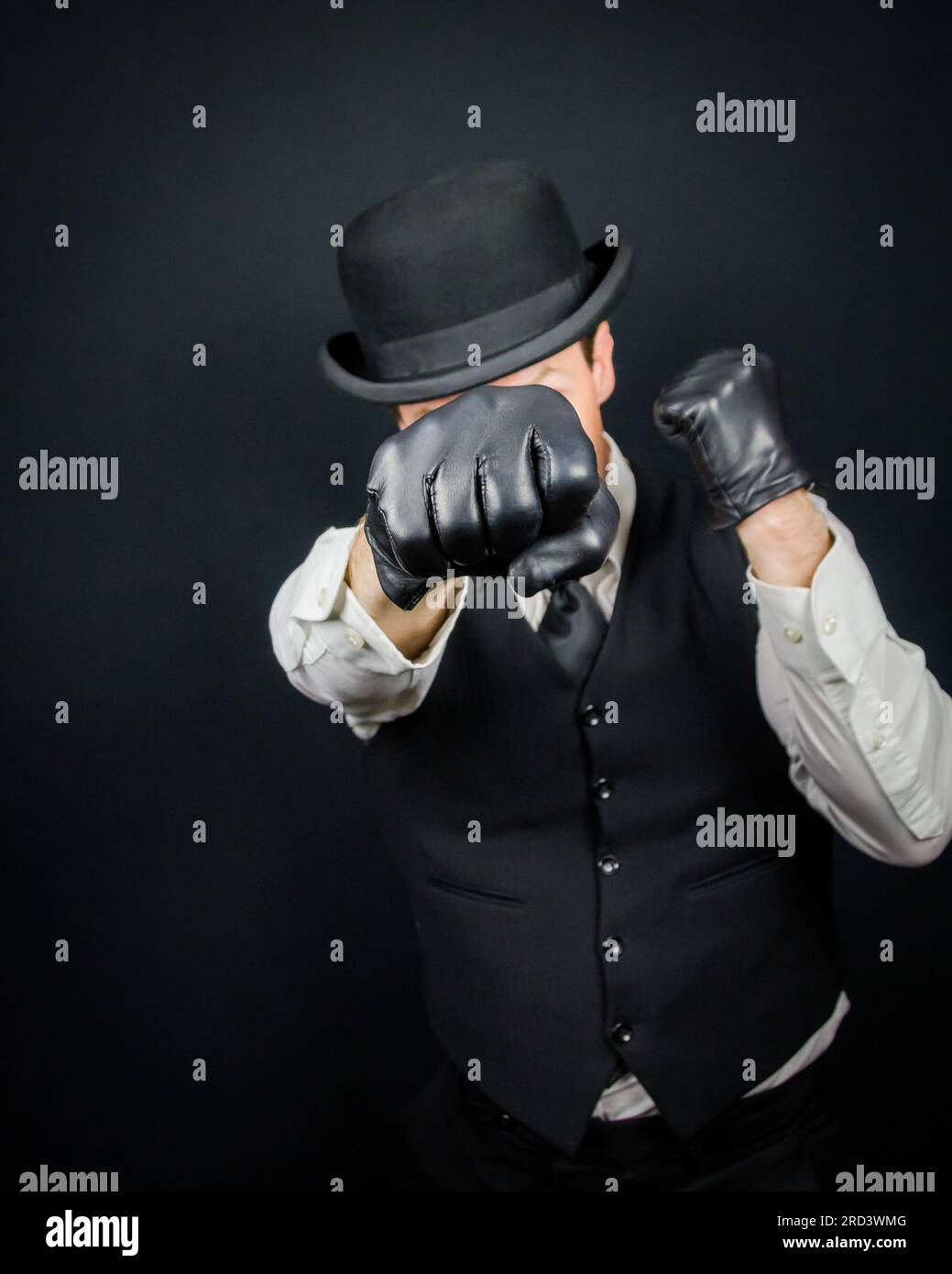 Portrait of Vintage Violent Criminal in Vest and Bowler Hat Throwing a Punch. Mobster in Black Leather Gloves. Stock Photo