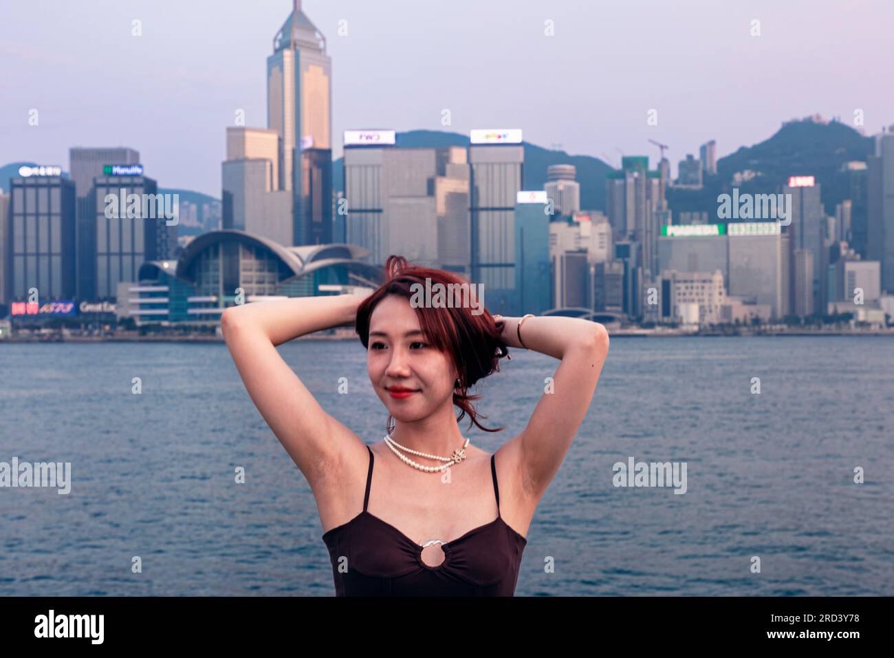 Young attractive Chinese girl posing for photo in front of Hong Kong  skyline, Victoria Harbour, Tsim Sha Tsui, SAR, China Stock Photo - Alamy