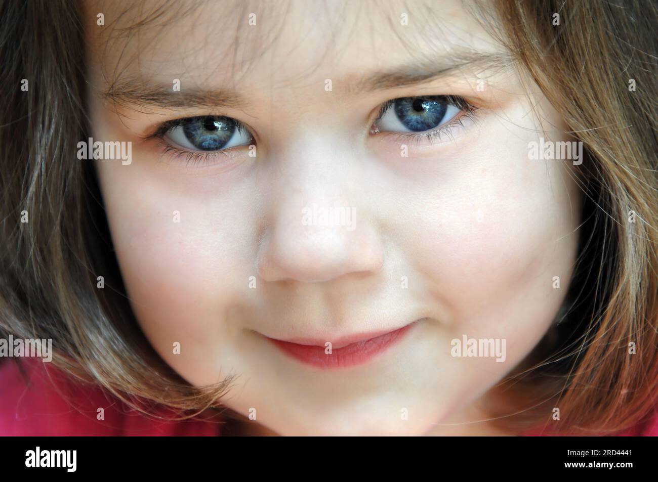 'Eyes of the Soul' are shown in this cropped closeup of a little girl's face.  She is giving an impish smile as she looks up. Stock Photo