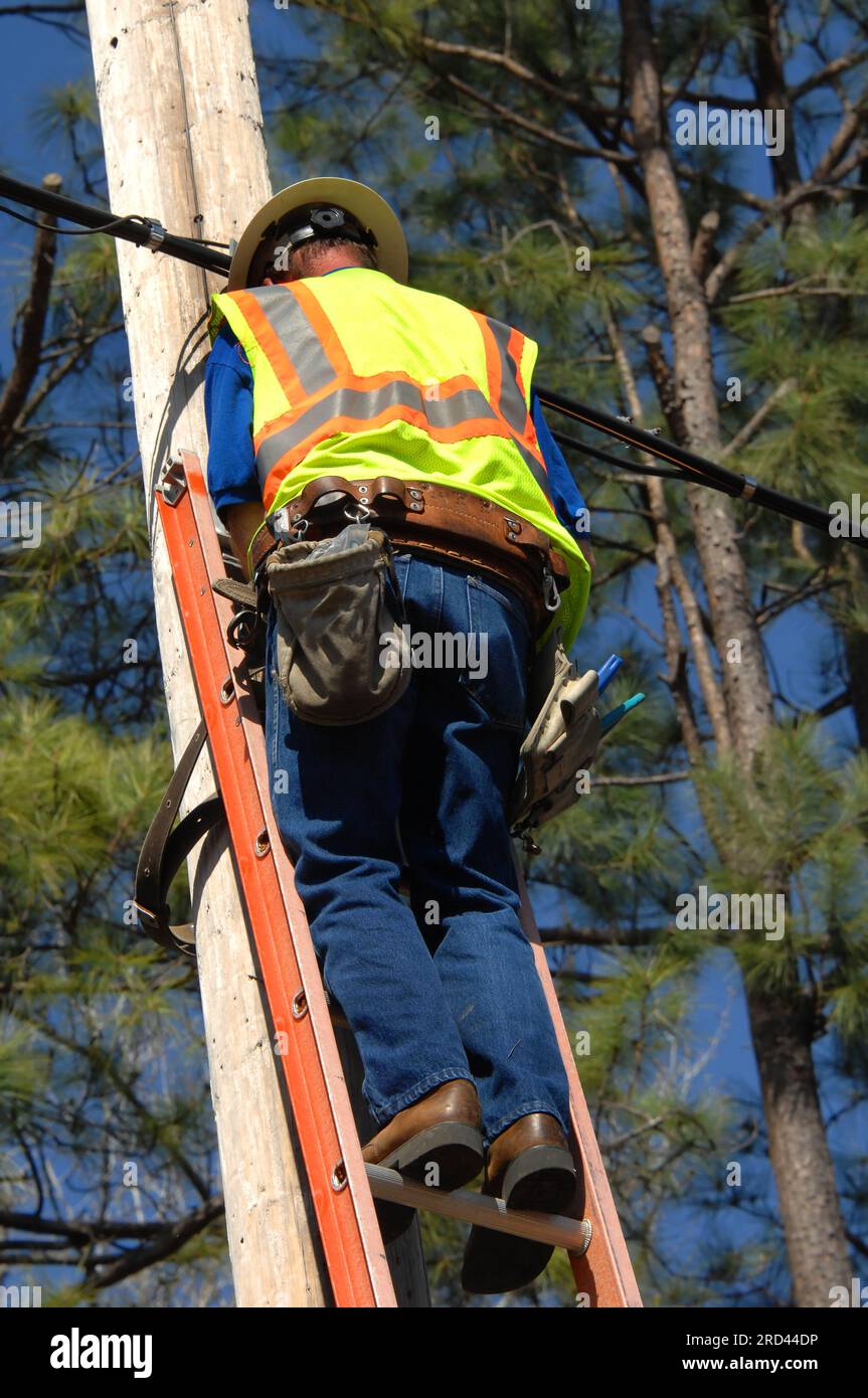 Employee works on power line on a sunny day with blue skies. He is ...