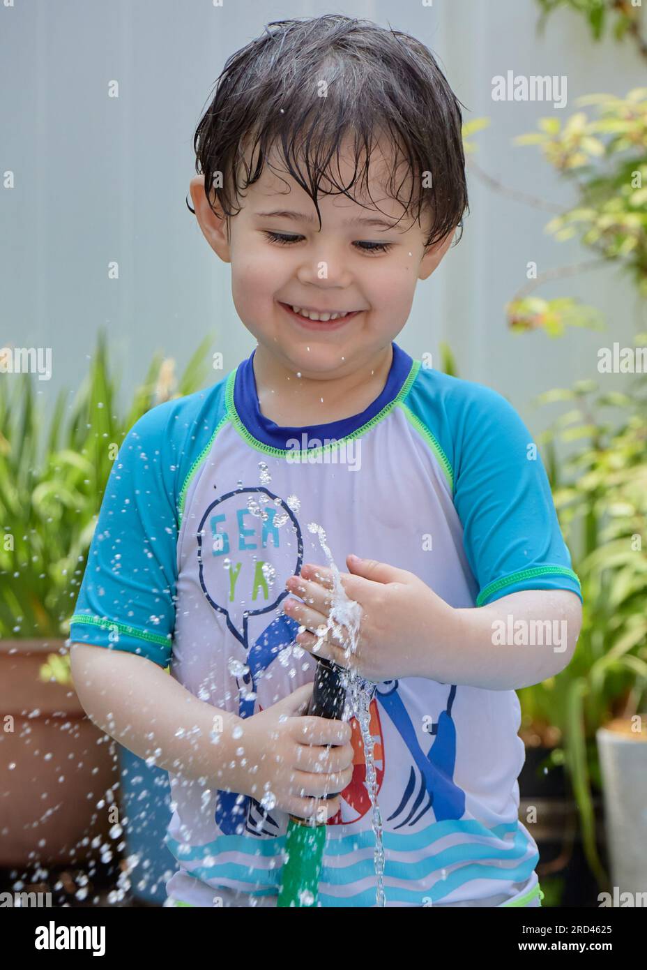 wet young boy in a bathing suit playing with a water hose in the backyard Stock Photo Alamy