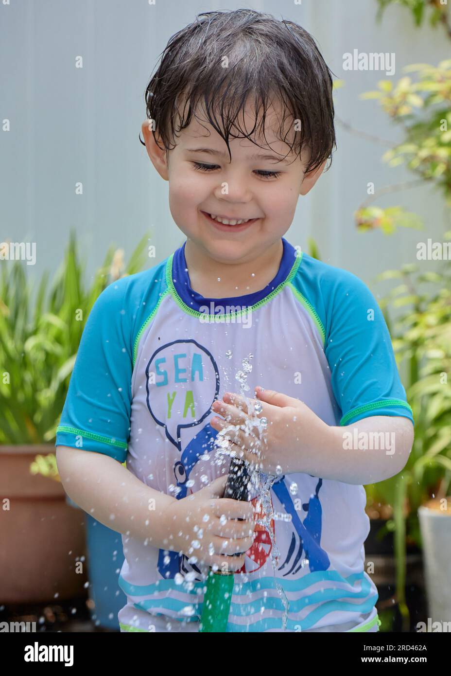wet young boy in a bathing suit playing with a water hose in the