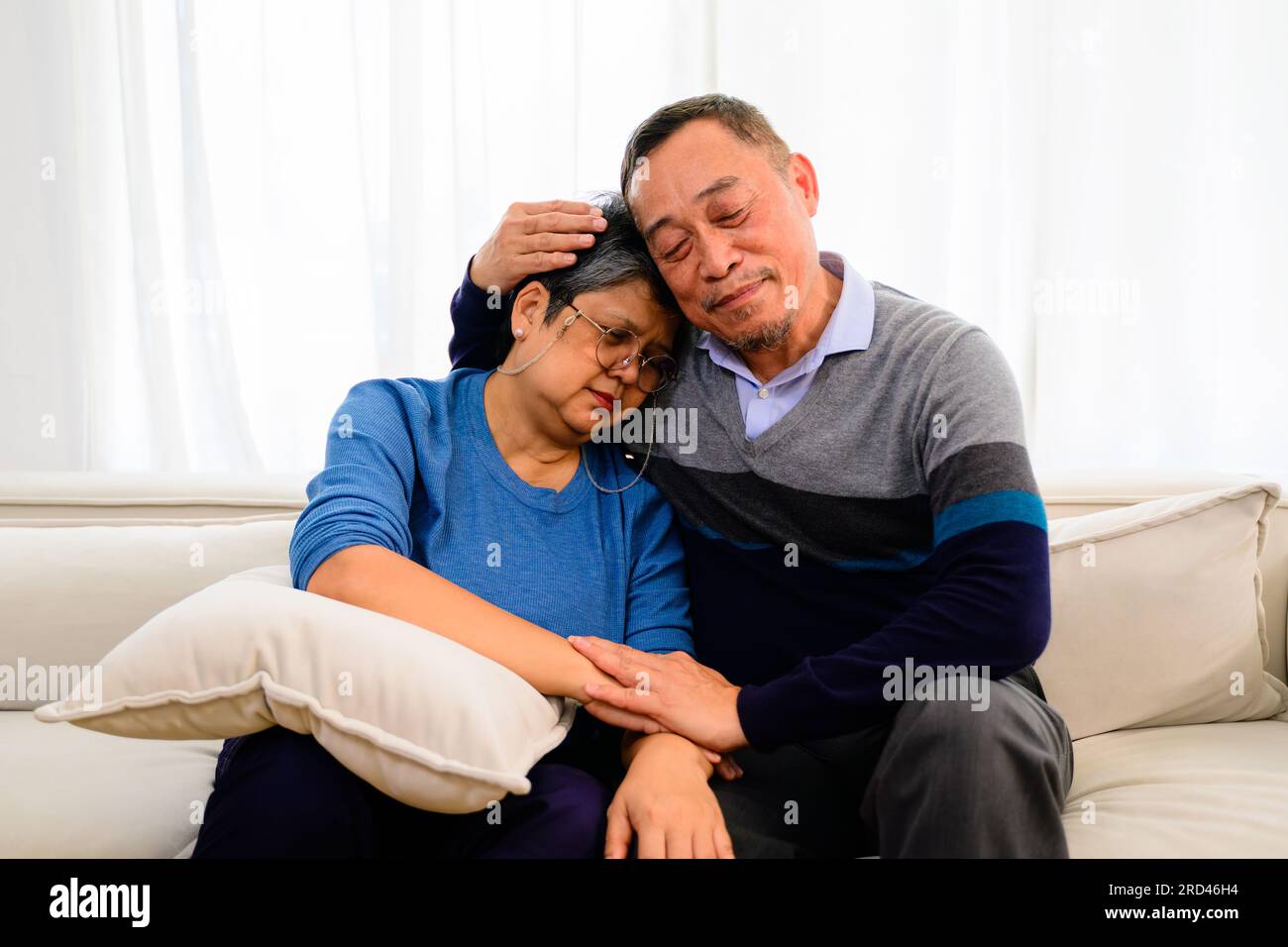 Portrait of healthy senior man and woman embracing and sitting on sofa at home, Happy senior married couple spending time in living room, Grandparents Stock Photo