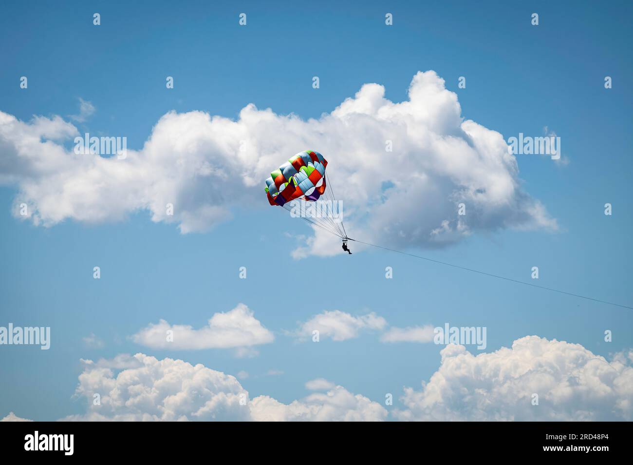 Silhouetted photo of a person parasailing in high in the clouds and blue sky. Stock Photo