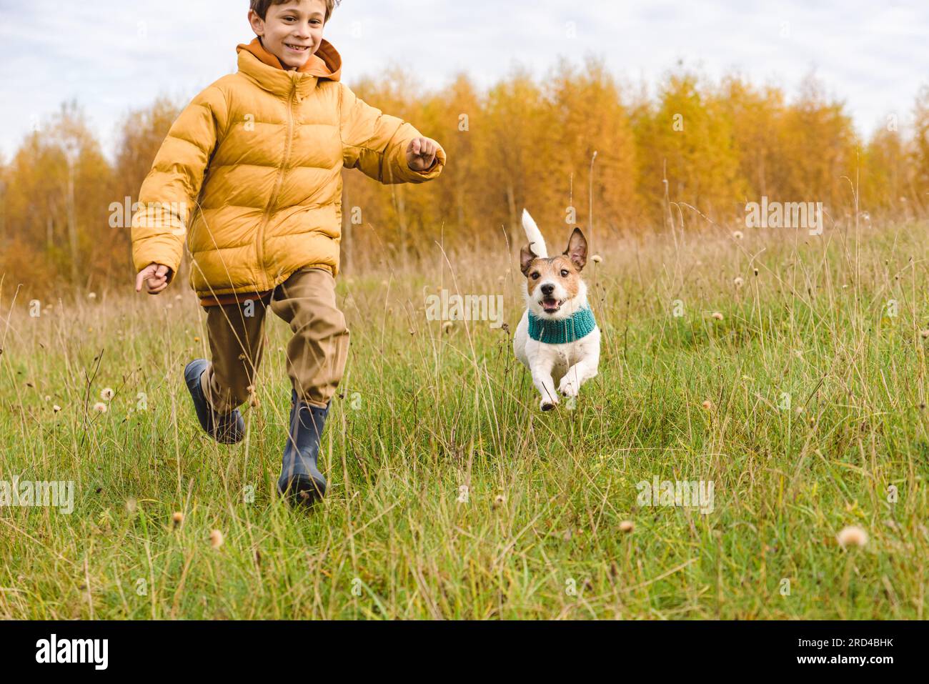 Happy smiling kid and his dog running and playing in Autumn meadow Stock Photo