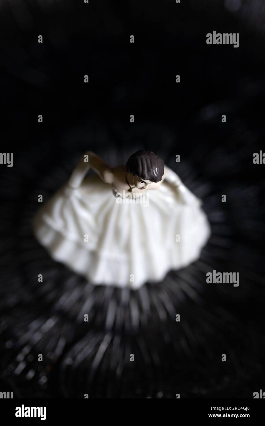 Plastic figurine of young woman in white gown, on a black background. Stock Photo
