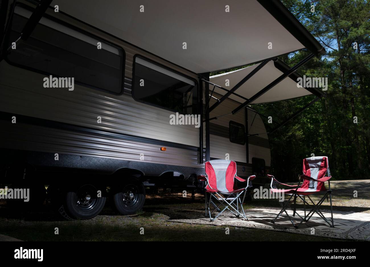 Red camping chairs under the awning of a travel trailer in a forested