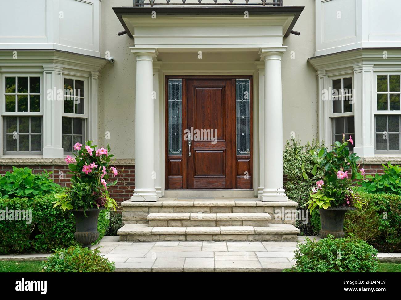 Elegant wood grain front door of home with portico entrance surrounded by flowers and shrubs