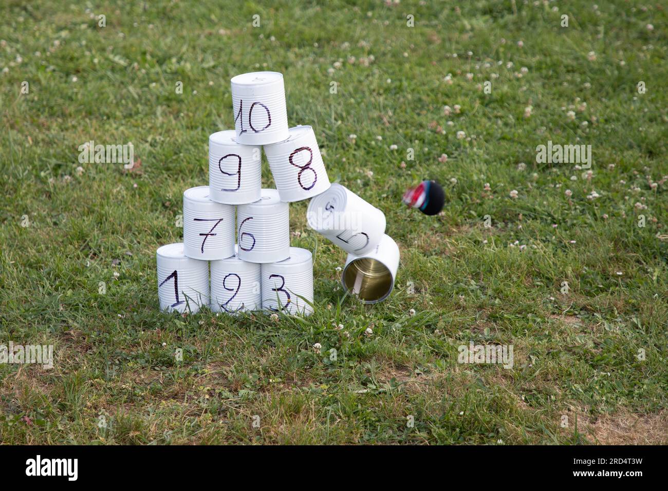 Friends playing knock falling down tin cans game throwing balls Stock