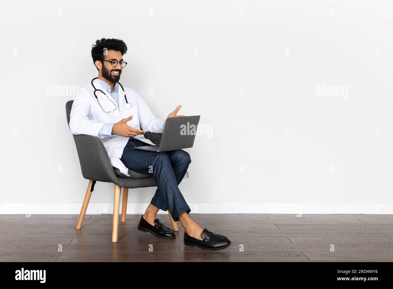 Handsome middle eastern young doctor sitting in armchair, using computer Stock Photo