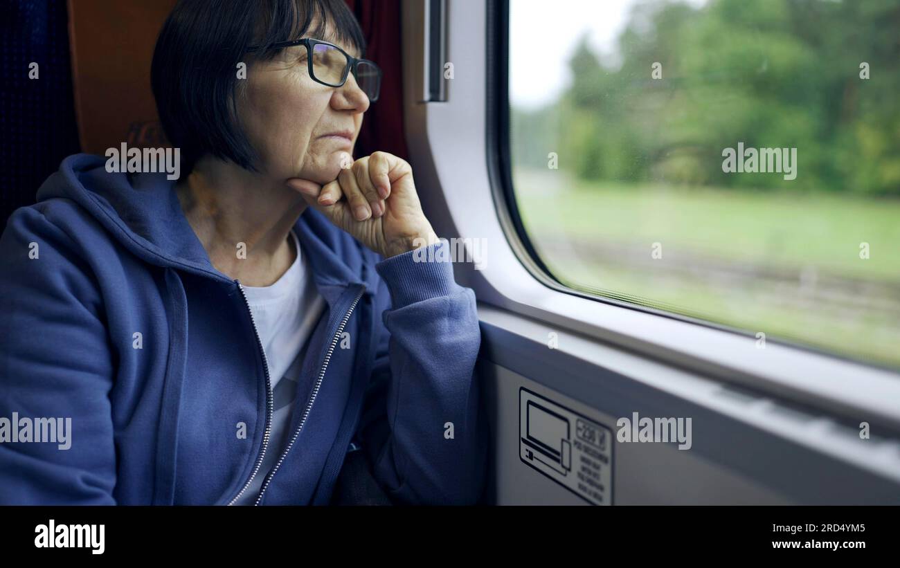 Elderly lady in glasses travels in train and looking out the window Stock Photo