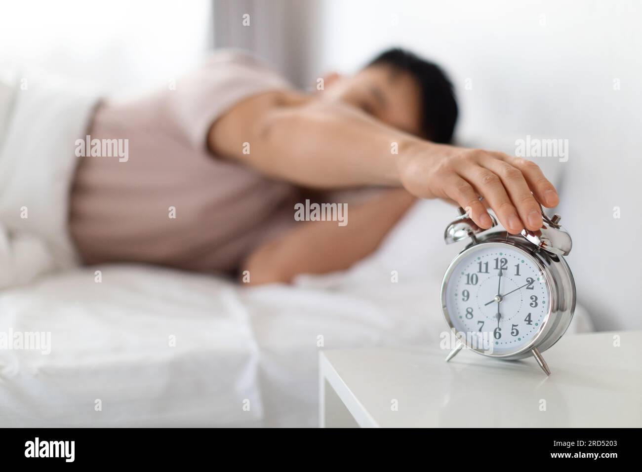 Asian man turning off alarm clock, waking up in morning Stock Photo