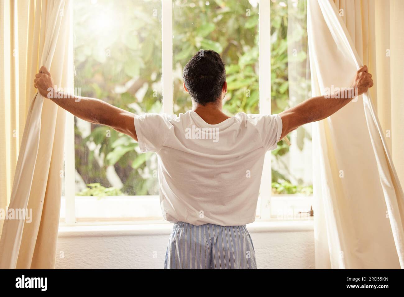 Back view, man and open curtain at window to good morning, sunrise and sunshine to relax in room