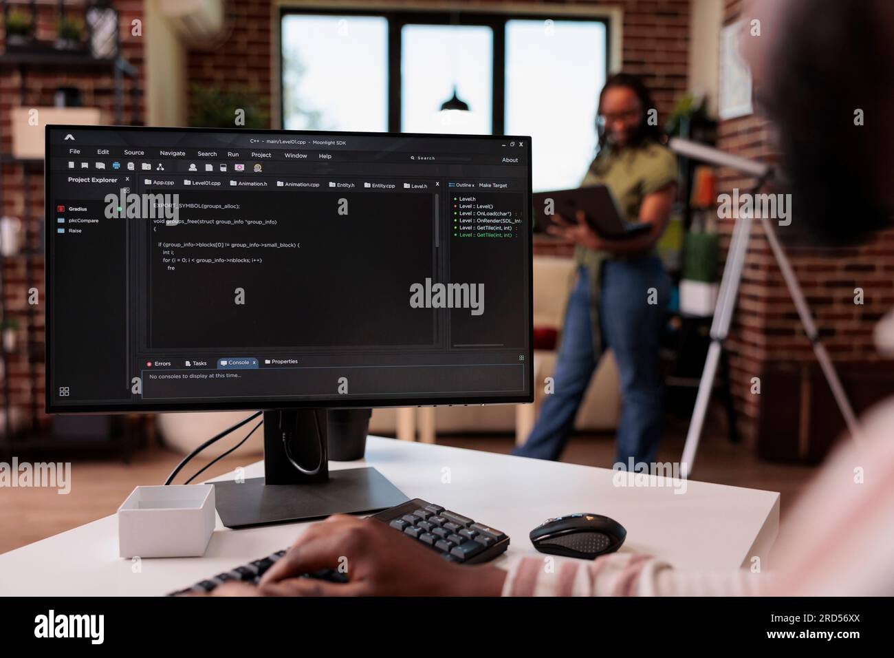 Freelance programmer developing source code on personal computer while girlfriend is using laptop standing in living room. African american couple working remote programming software together. Stock Photo