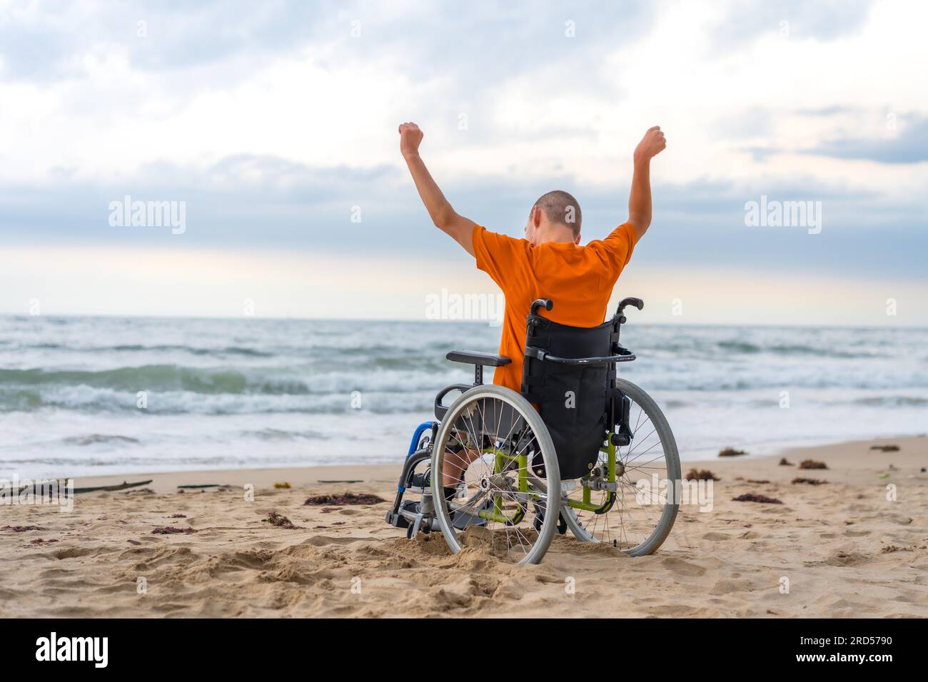 Disabled person on his back in a wheelchair on the beach with open arms