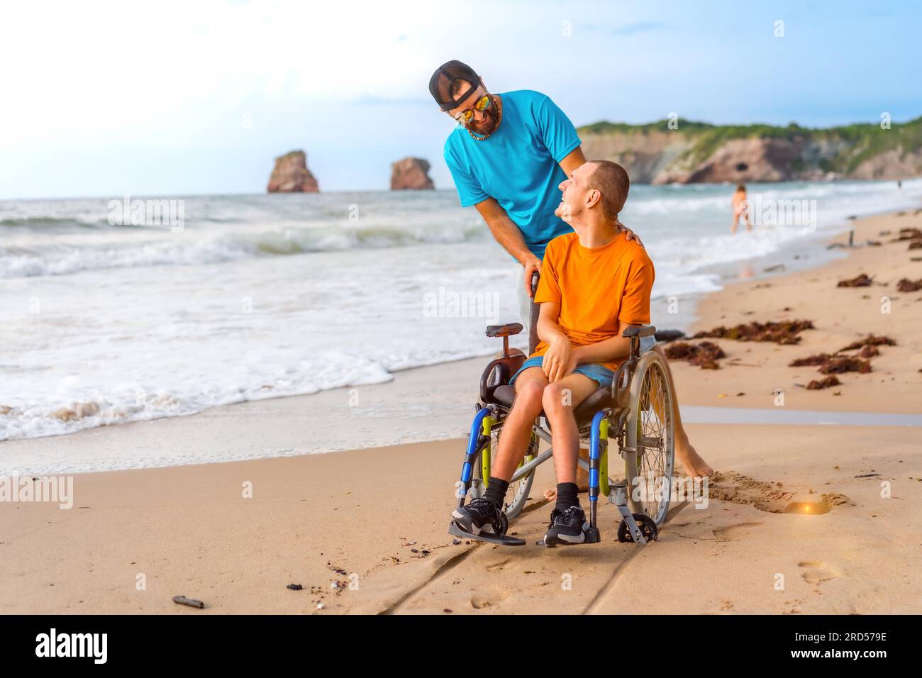 A disabled person in a wheelchair on the beach pushed by a friends by ...