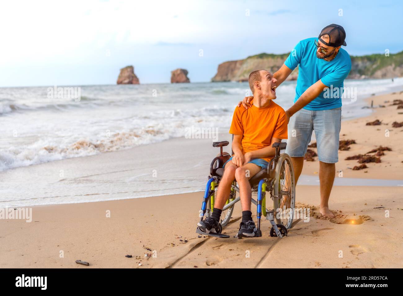 A disabled person in a wheelchair on the beach pushed by a friends by
