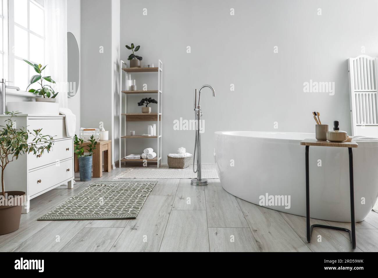 Interior of light bathroom with bathtub, table and chest of drawers