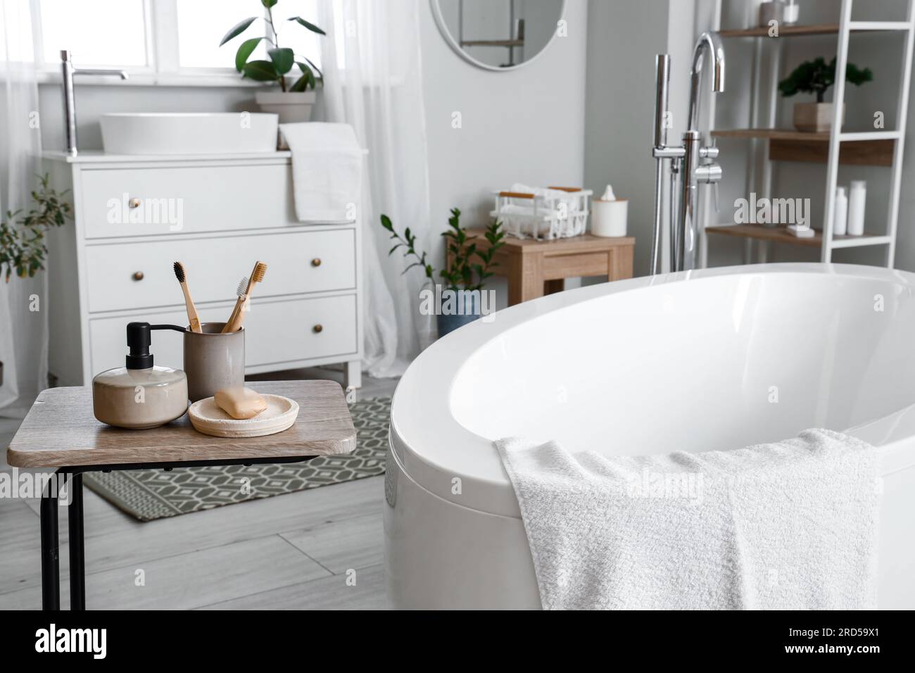 Interior of light bathroom with bathtub, table and chest of drawers