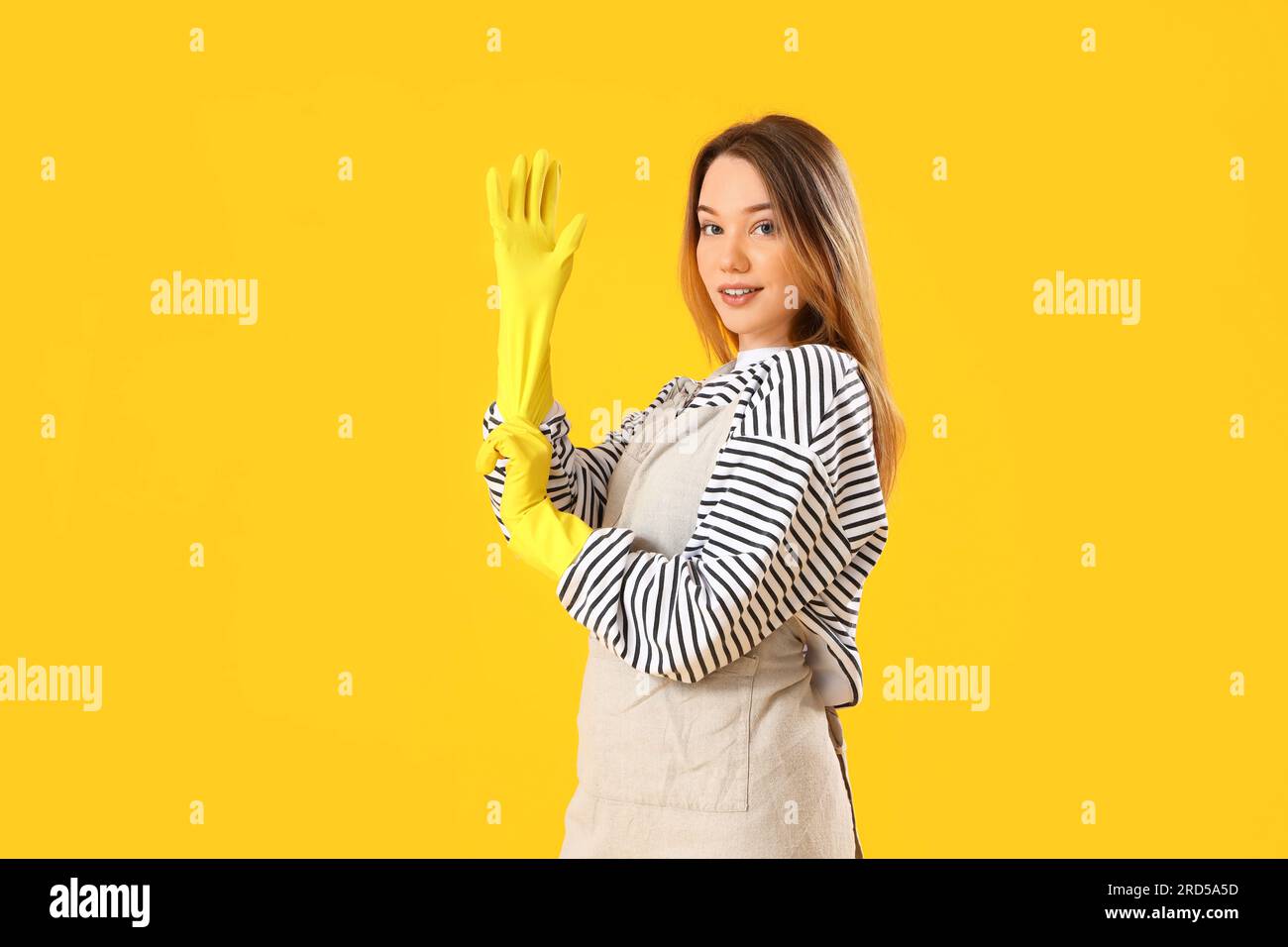 Young woman putting rubber gloves on yellow background Stock Photo - Alamy