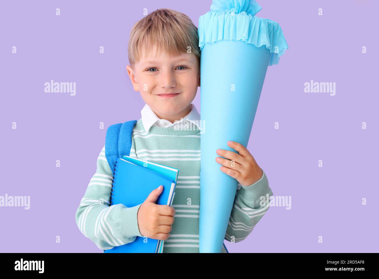 Happy little boy with backpack, blue school cone and notebooks on lilac background Stock Photo