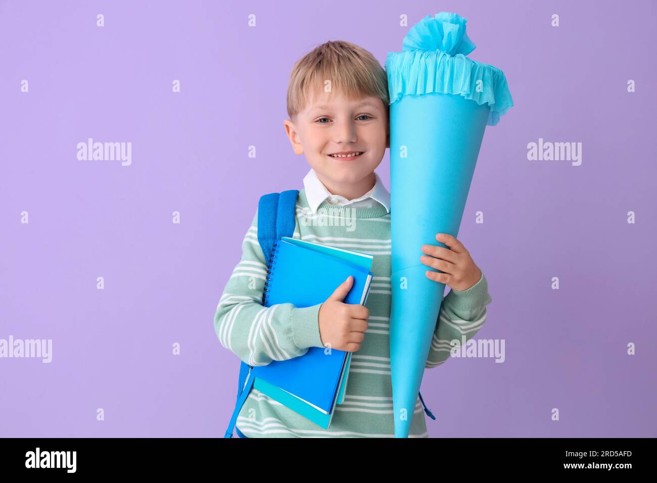 Happy little boy with backpack, blue school cone and notebooks on lilac background Stock Photo