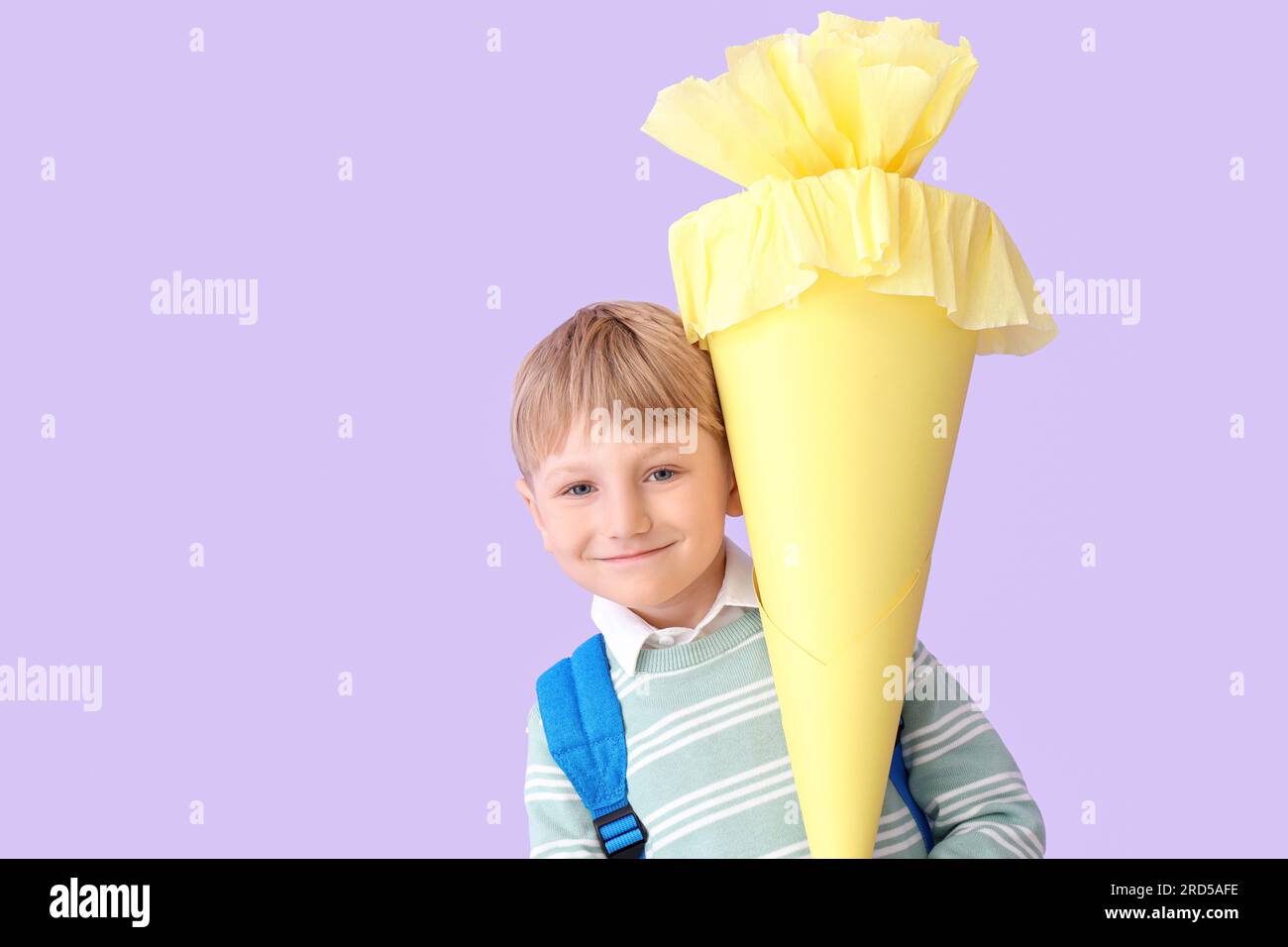 Happy little boy with backpack and yellow school cone on lilac background Stock Photo